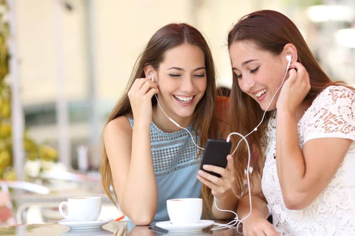 Friends sharing and listening to music with earphones and smartphone in a coffee shop
