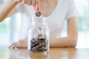 Woman Dropping Coins Into Glass Jar